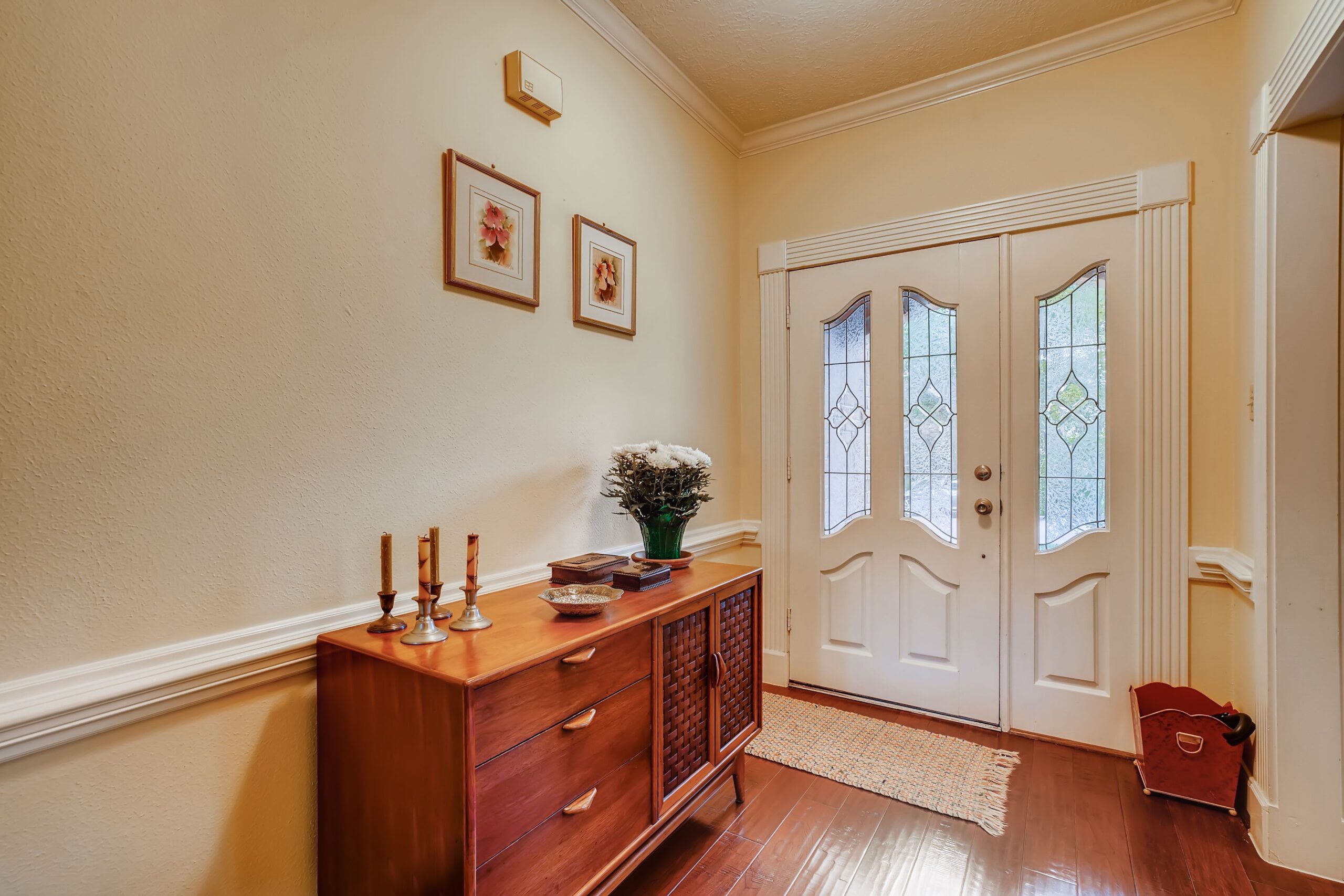Foyer before: walnut credenza with small framed prints hung high, cluttered tabletop and a small rag rug