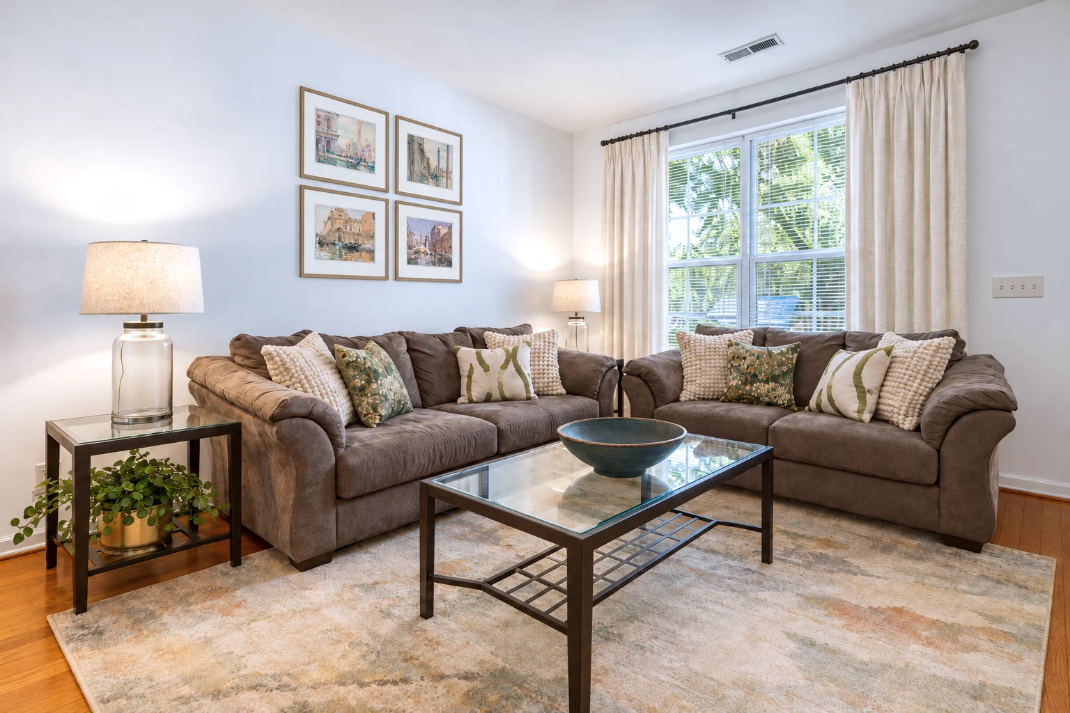 The same living room after, with the same sofas, a soft rug, cream curtains and framed watercolors